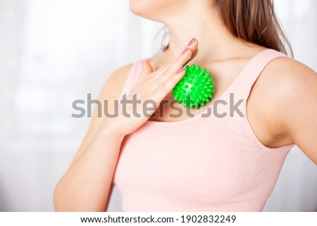 Close-up young woman in a pink top massages her cleavage and neck with a green spiky ball.