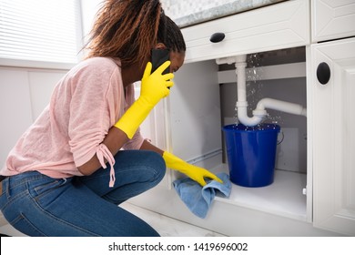 Close-up Of A Young Woman Placing Blue Bucket Under Water Leaking From Sink Pipe