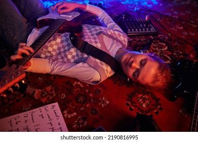 Closeup of young woman playing guitar while lying on carpet lit by dim red lights - Powered by Shutterstock