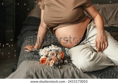 Close-up of young woman with pregnant belly. Attractive pregnant woman with large tummy sitting on the bed and waiting for a newborn baby. Concept of pregnancy, motherhood, procreation, expectation