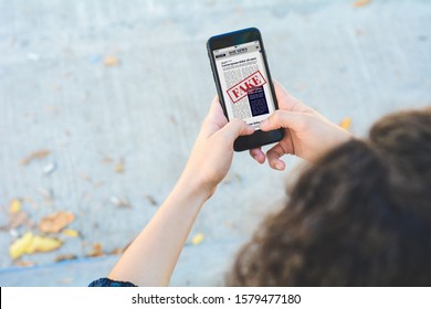 Closeup Of Young Woman Reading Digital Fake News On Smartphone. Propaganda And Disinformation Online. Media And Digital Concept. All Screen Graphics Are Made Up By Us

