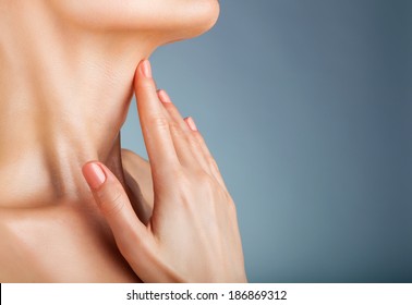 Closeup Of A Young Woman Regards Her Neck On A Gray Background