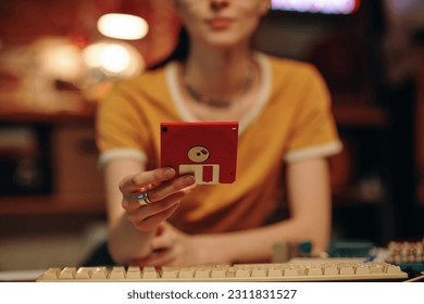 Close-up of young woman saving information on floppy disk while working on computer