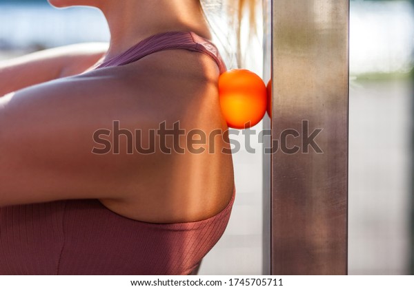 Closeup young woman shoulders in tight top\
leaning on small ball against wall to fix back ache, massaging\
stiff muscles and sore neck, exercise to relieve spinal pain.\
Relaxation and muscle\
stretching
