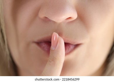 Close-up of young woman showing shh gesture or to keep silent sign. Female holding finger near lips. Quiet place and silence time concept