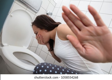 Close-up Of A Young Woman Showing Stop Sign While Vomiting In Toilet Bowl