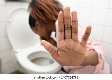 Close-up Of A Young Woman Showing Stop Sign While Vomiting In Toilet Bowl