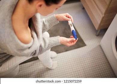Close-up of young woman sitting in bathroom and checking result of pregnancy test, she waiting for result on small display