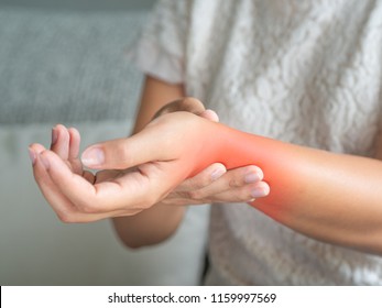 Closeup Young Woman Sitting On Sofa Holds Her Wrist. Hand Injury, Feeling Pain. Health Care And Medical Concept.