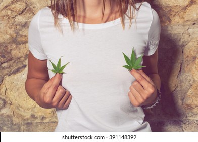 Closeup of young woman sitting outside and holding cannabis green leaves in her hands