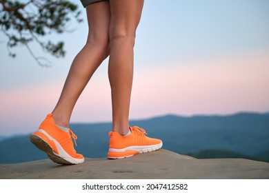 Closeup of young woman slim legs in bright orange sneaker shoes walking on mountain hiking trail in summer. Active way of life and exercise on fresh air concept.