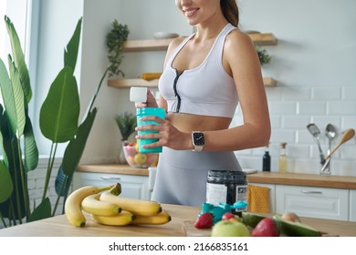 Close-up of young woman in sports clothing preparing protein cocktail at home - Shutterstock ID 2166835161