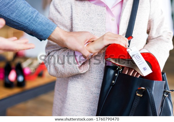 Closeup of young woman is stealing red shoes in\
store, shop, boutique at shopping center. Girl is hiding unpaid\
good in handbag. Seller, assistant caught thief on hot. Shoplifting\
concept.