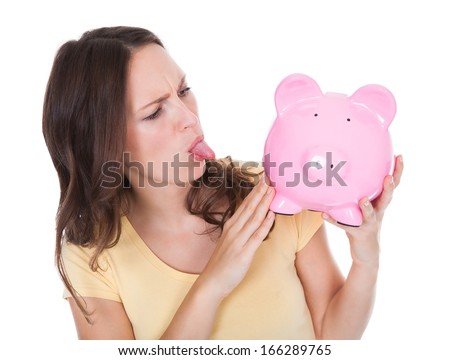 Close-up Of A Young Woman Sticking Tongue Out Looking At Piggybank