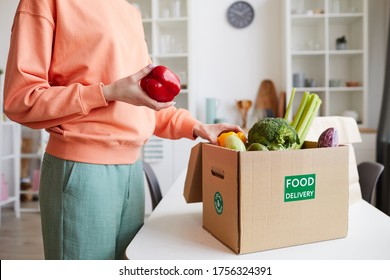 Close-up of young woman unpacking the fresh vegetables from the box while standing in domestic kitchen