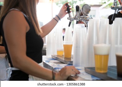 closeup of a young woman while she's working at the beer tap. she is tapping a blonde beer in a plastic glass during a spring festival.  - Powered by Shutterstock