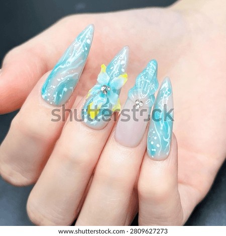 Close-up of a young woman's hand featuring long oval acrylic nails with trendy ocean-inspired nail art. Summer nail