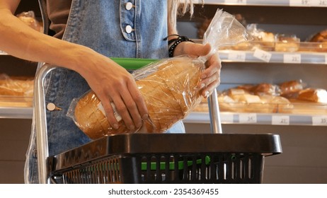 Close-up of a young woman's hands putting a package of sliced long loaf into a shopping cart - Powered by Shutterstock