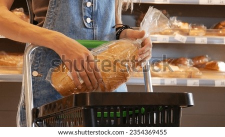 Close-up of a young woman's hands putting a package of sliced long loaf into a shopping cart