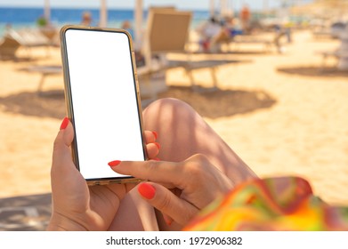 Closeup of young woman's hands using white mobile smartphone Mockup on the beach, beach resort and Sea in the background. woman holding mobile phone with blank desktop screen while sitting on beach