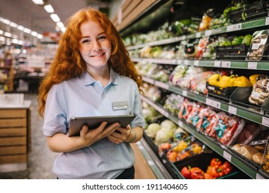 Closeup Of A Young Worker With Digital Tablet In Grocery Store. Happy Trainee Working In Supermarket.