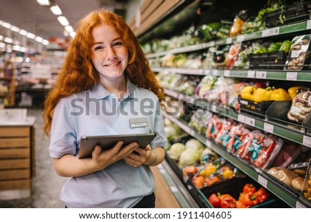 Closeup of a young worker with digital tablet in grocery store. Happy trainee working in supermarket.