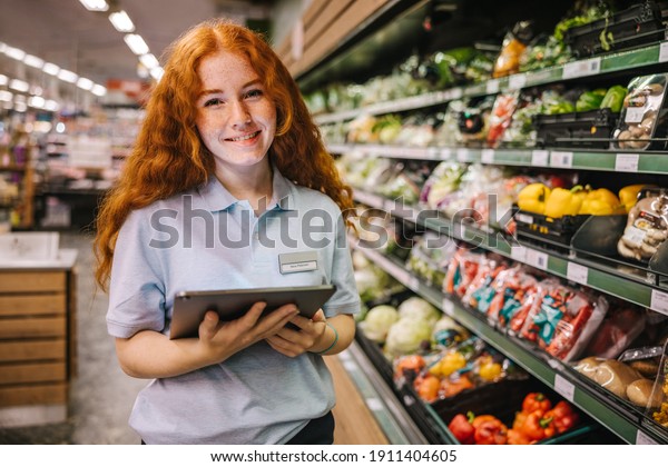 Closeup of a young worker\
with digital tablet in grocery store. Happy trainee working in\
supermarket.