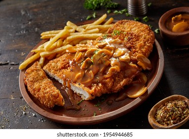 Closeup of yummy fried breaded pork escalope garnished with traditional aromatic chasseur sauce with mushrooms served with French fries on rustic wooden table