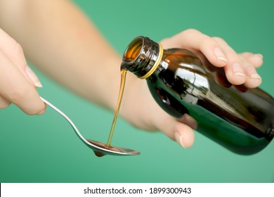 Close-ups of a hand pouring syrup into a spoon from a bottle of cough, infection and sore throat medicine. Healthcare concept 