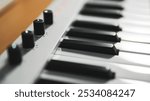 Closeups of a piano, midi controller, or keyboard with adjustable knob on a wooden table. Home studio or music equipment concept.