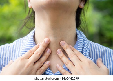 Closeup,Sick woman suffering from sore throat,painful swallowing,tonsillitis,irritation,asian female patient checking thyroid gland by herself,holding hand on her neck in outdoor,laryngitis,healthcare