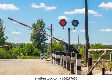 A  closing barrier and red traffic light at the railway crossing. railway station.