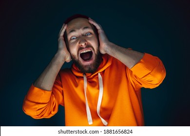 Closing Ears. Portrait Of Crazy Scared And Shocked Caucasian Man Isolated On Dark Background. Copyspace For Ad. Bright Facial Expression, Human Emotions Concept. Watching Horror On TV, Cinema.