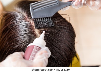 Closu-up Of Hair Dresser Applying Chemical Hair Color Dye Onto Hair Roots In Salon