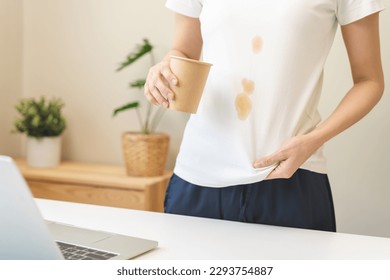 Cloth stain, disappointment asian young woman clumsy with hot coffee, tea stains on shirt, hand show making spill drop on white t-shirt, spot dirty or smudge on clothes at home, isolated on background - Shutterstock ID 2293754887