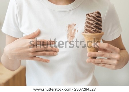 Cloth stain, disappointment asian young woman, girl eating melting ice cream in waffle cone on hot weather, hand show making chocolate cream drop on white t-shirt, spot dirty or smudge on clothes.