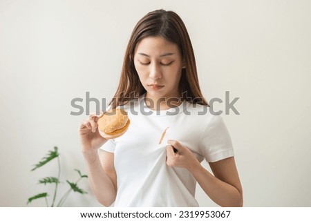 Cloth stain, disappointment asian young woman, girl eat food hand hold hamburger, burger show making tomato sauce smudged spilling, drop on white t-shirt, spot dirty or smudge on clothes, dirt stains.
