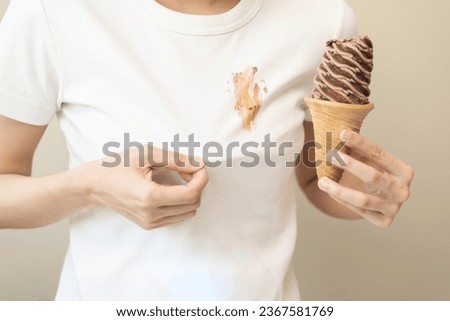 Cloth stain, disappointment asian young woman, girl eating melting ice cream in waffle cone on hot weather, hand show making chocolate cream drop on white t-shirt, spot dirty or smudge on clothes.
