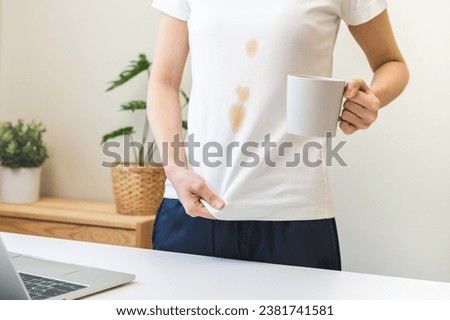 Cloth stain, disappointment asian young woman, girl clumsy with hot coffee, tea stains, hand show making spill drop on white t-shirt, spot dirty or smudge on clothes while working on computer at home.