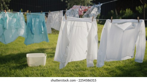 Clothes and bedding are drying in the backyard of the house, a laundry basket is standing on the grass nearby. - Powered by Shutterstock