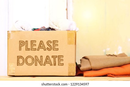 Clothes In Carton Box On Wood Table For Donation, Coat Drive Concept, Please Donate Text