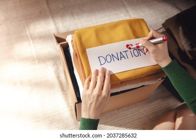 Clothes Donation Concept. Box Of Cloth With Donate Label. Woman Preparing Used Old Garment At Home. Top View