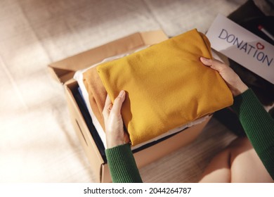 Clothes Donation Concept. Box Of Cloth With Donate Label. Woman Preparing Used Old Garment At Home. Top View