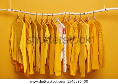 Clothes hanger filled with solid yellow female sweaters. One white sweater stands out of collection, being on sale. Wide choice on clothing in store. Big assortment. Black Friday and discounts