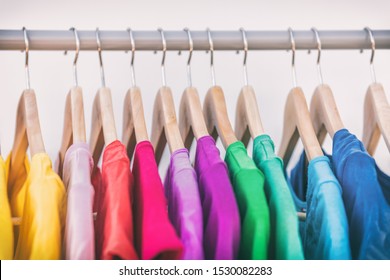 Clothes hanging on clothing rack wardrobe fashion apparel selection of rainbow color t-shirts on closet hangers. Womens wear in store shopping spring cleaning concept. Summer home wardrobe.