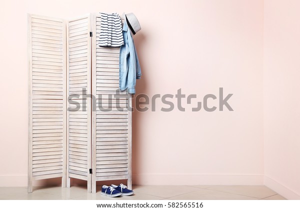 Clothes\
hanging on folding screen on a beige\
background
