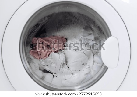 Clothes inside washing machine drum during laundry cycle preparation. Mixed garments and fabrics in household washer. Daily home chores and cleaning routine. Domestic appliance interior close-up view
