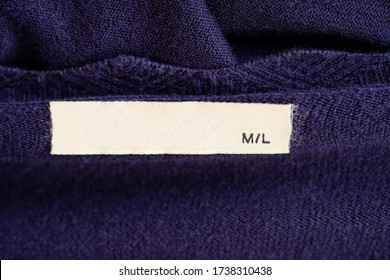 Clothes Label On Purple Textile Background Closeup. Blank White Clothes Label On Knitted Sweater.  Cloth Label  Blank Mockup Rectangular On A Collar With Size M/L