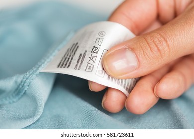 Clothes, Laundry, People And Housekeeping Concept - Close Up Of Hand Holding Label With Users Manual Of Clothing Item