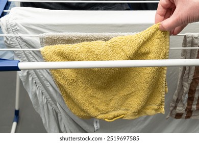 Clothes on drying  rack, full of laundry. Hand is picking a dry towel to stow  it away.